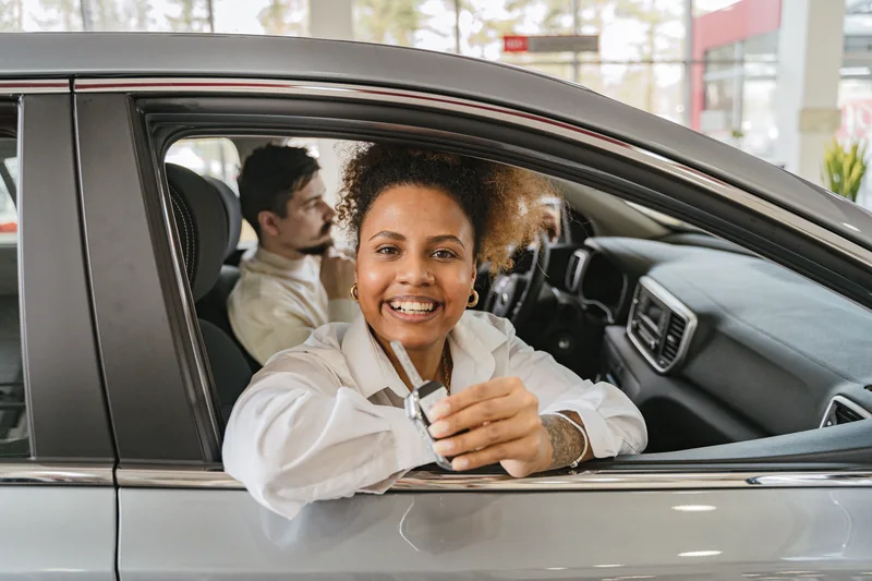 A smiling shopper seated in a car and holding its key