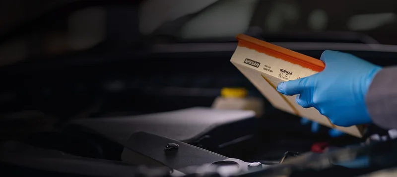 Gloved hand inspecting a Nissan engine air filter