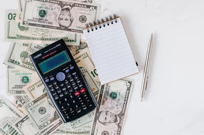 A notebook, calculator, pen, and US dollar bills for budget planning