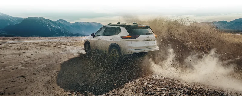 Rear three-quarter view of a white Rogue driving through mud