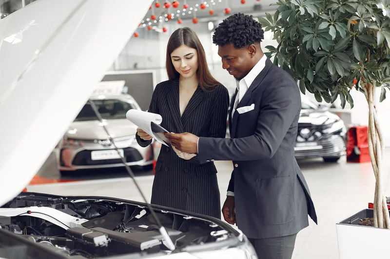 A shopper and salesperson examining a vehicle with its hood open
