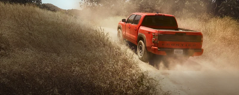 Orange Frontier PRO-4X driving away through dust on a rugged trail