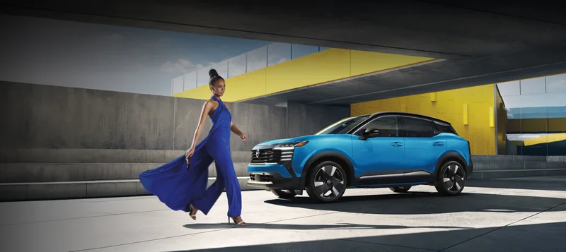 Blue Kicks parked at a modern concrete building with a pedestrian nearby