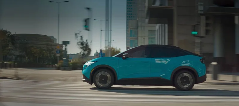 Blue third-generation 2026 LEAF driving through a city intersection