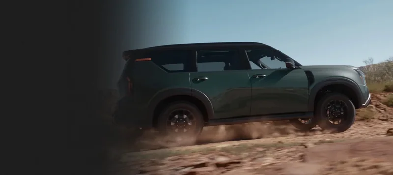 Green Armada PRO-4X in side/front-three-quarter view driving through desert terrain