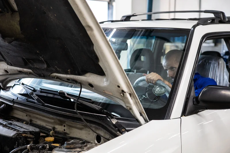 A mechanic inspecting an older vehicle with its hood open