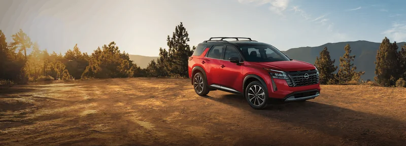 Red refreshed Pathfinder parked on a countryside road beside autumn foliage